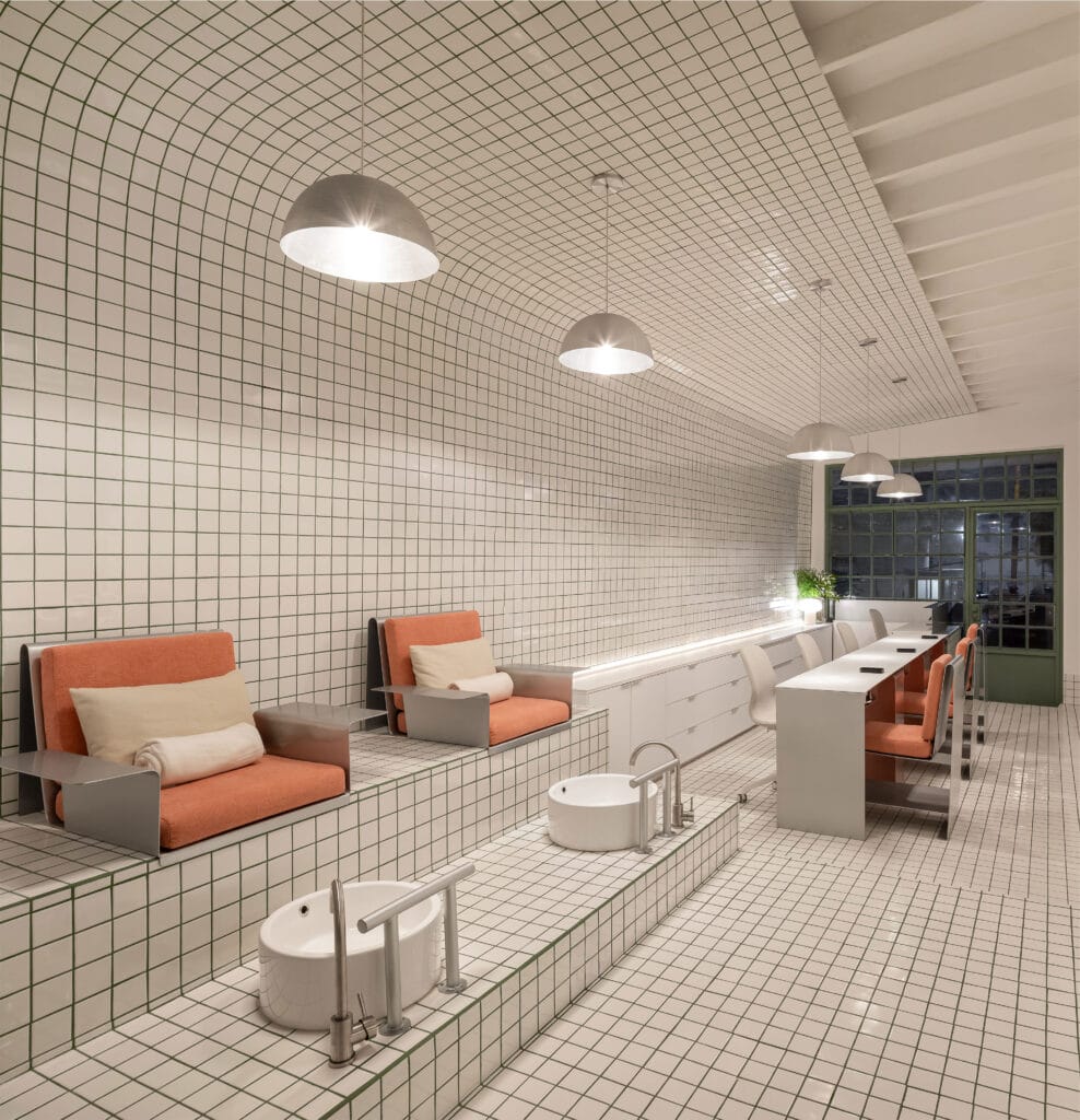 A nail salon with white tiled walls that resemble a subway and bright orange chairs.