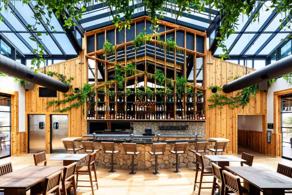 The interior of a farm-to-table restaurant with a glass roof and decorated with plants and greenery.