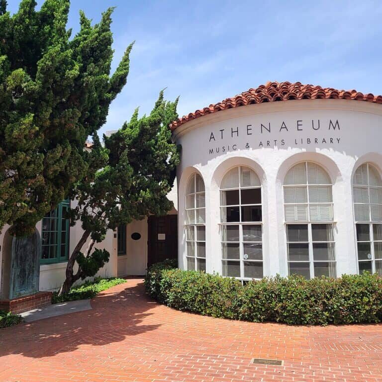 An off-white building with a red tiled roof featuring arched windows and a nicely landscaped patio area.