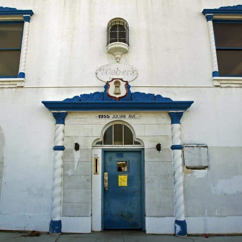 The outside of Bread & Salt presents as an older, white building with a blue door and blue trimmed awning.