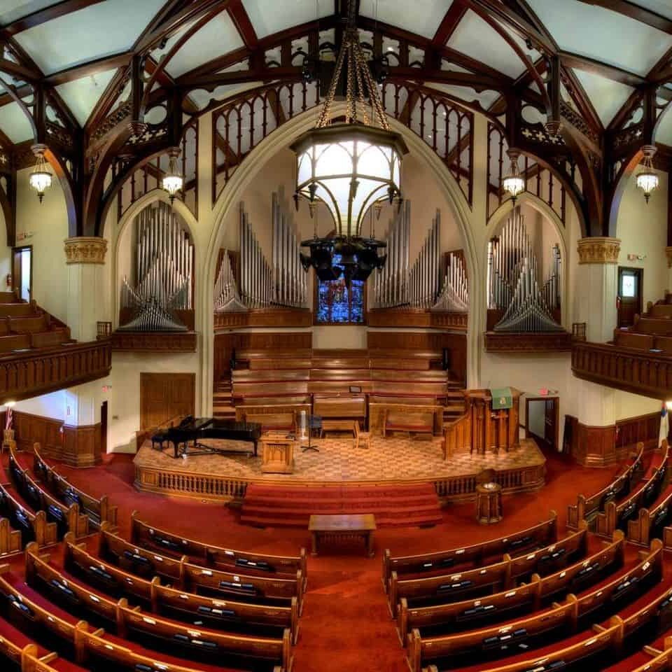 Elegant church interior with high ceiling, exposed wooden beams, dark wood pews, and a rich red carpet.