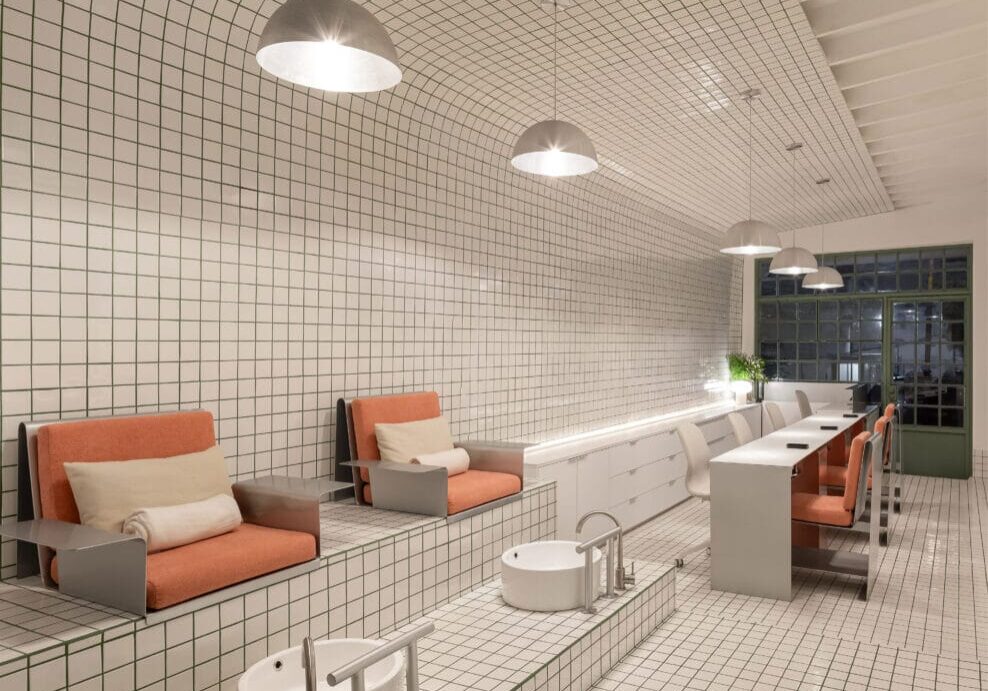 A nail salon with white tiled walls that resemble a subway and bright orange chairs.