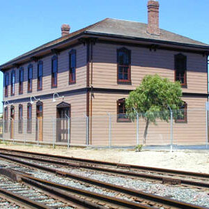 A large brown building sits next to a set of train tracks. The building is over 140 years old.