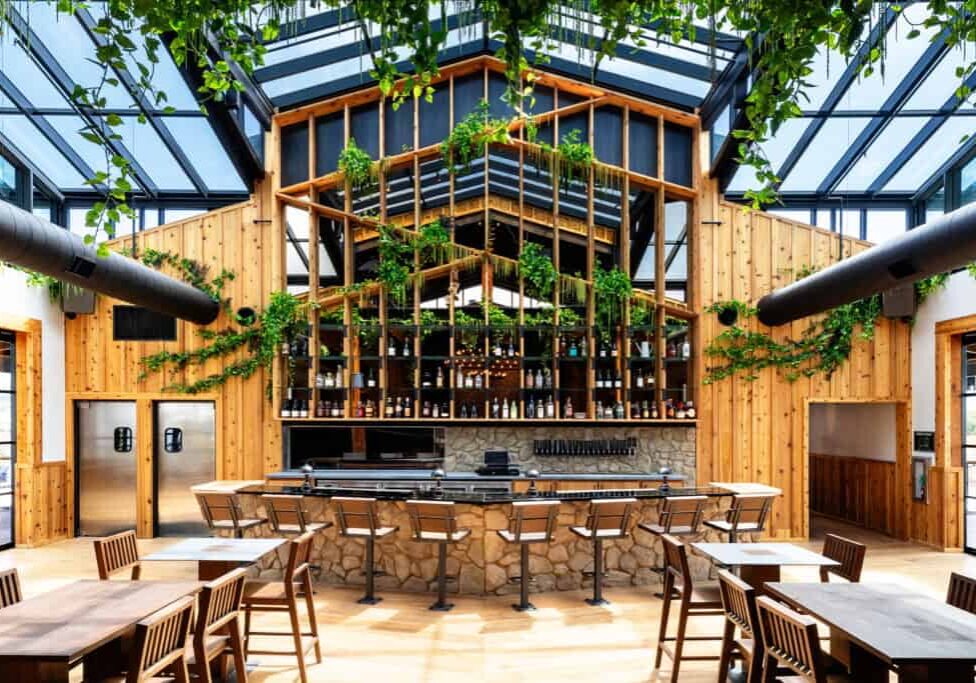 The interior of a farm-to-table restaurant with a glass roof and decorated with plants and greenery.