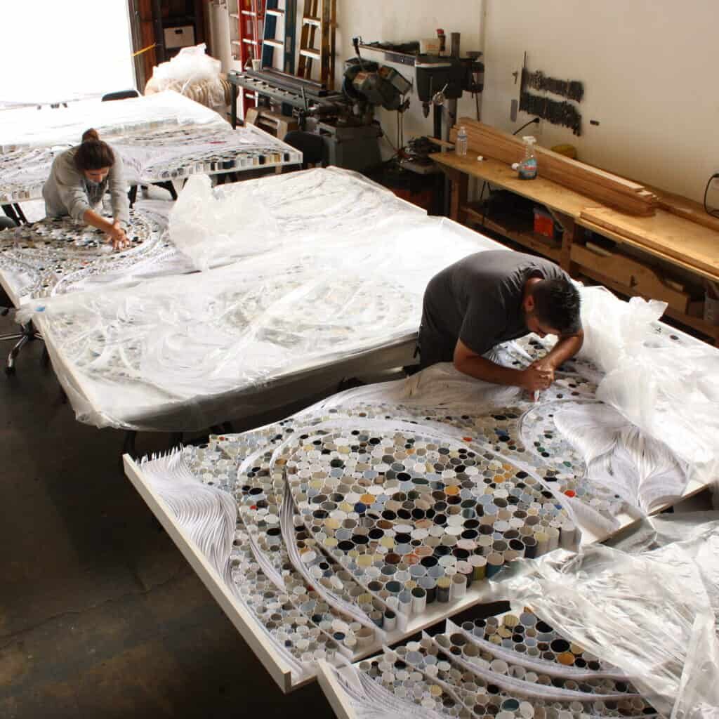 Two artists work on large mosaics made of stones at the Tecture space.