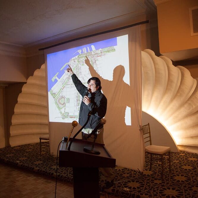 A person stands on stage presenting their slides for PechaKucha Night